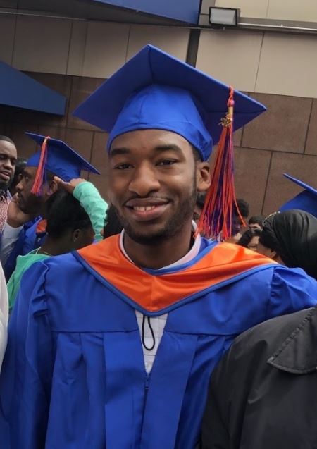 Photo of the intern as a graduate, wearing blue mortarboard and gown with orange tassel and stole